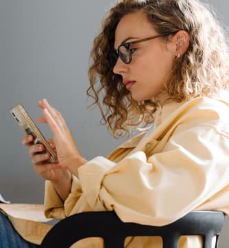 Mulher usando smartphone em um ambiente de trabalho, simboliza o acesso à informação e a importância de canais de denúncias institucionais para promover a transparência, a ética e a responsabilidade nas organizações.
