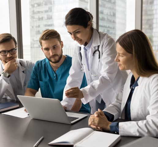 Equipe médica reunida analisando informações em um laptop, destacando temas institucionais relacionados a acesso à informação, qualidade e segurança no ambiente hospitalar, para promover decisões baseadas em dados e excelência no atendimento.