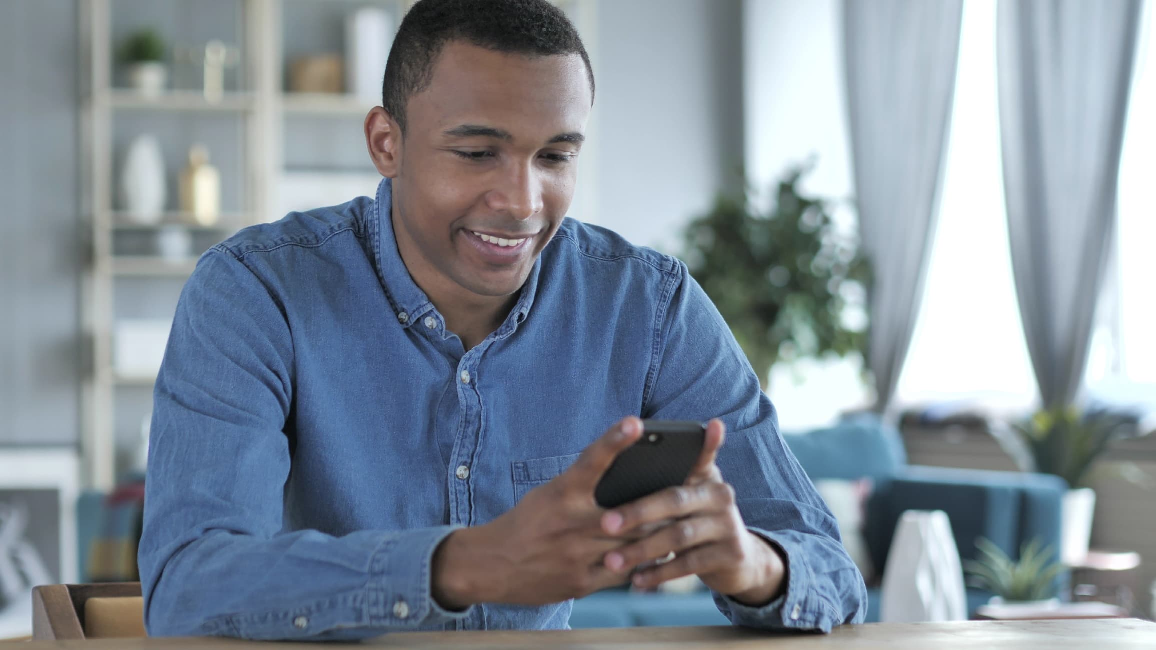 Homem jovem com camisa azul olha seu celular e sorri. Ele entra no site do Einstein, faz seu cadastro e demonstra confiança nos serviços oferecidos e na forma como o hospital protege seus dados pessoais