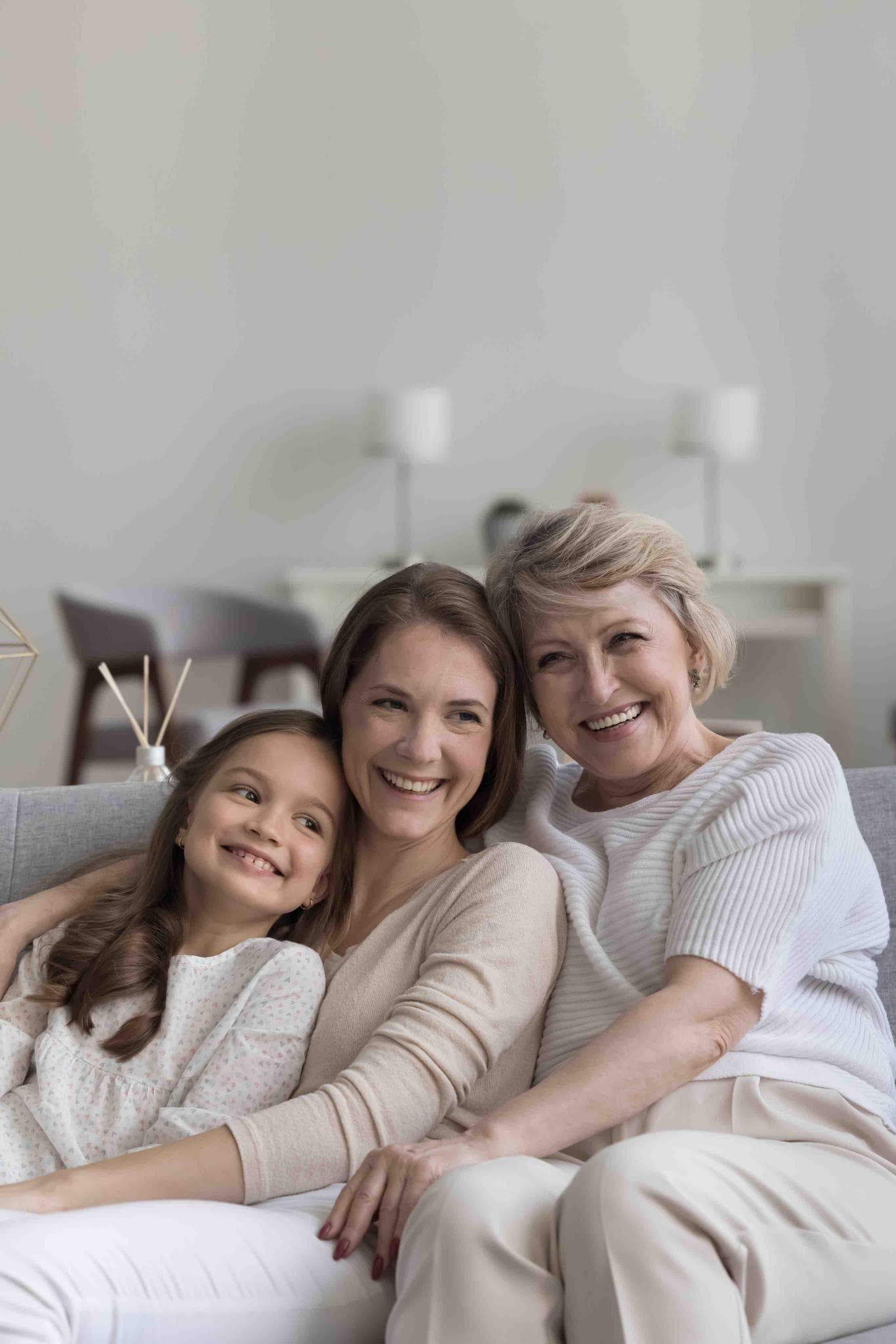 Criança, mulher e idosa sorrindo juntas em casa, representando bem-estar e saúde mental em diferentes fases da vida