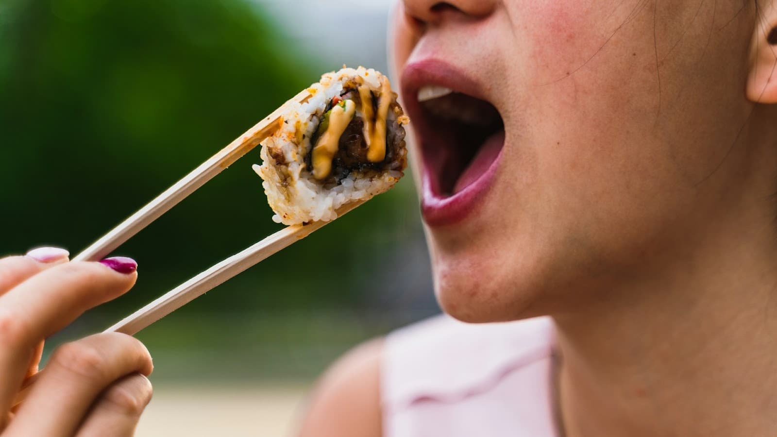 Pessoa comendo comida japonesa com hashi em um ambiente ao ar livre