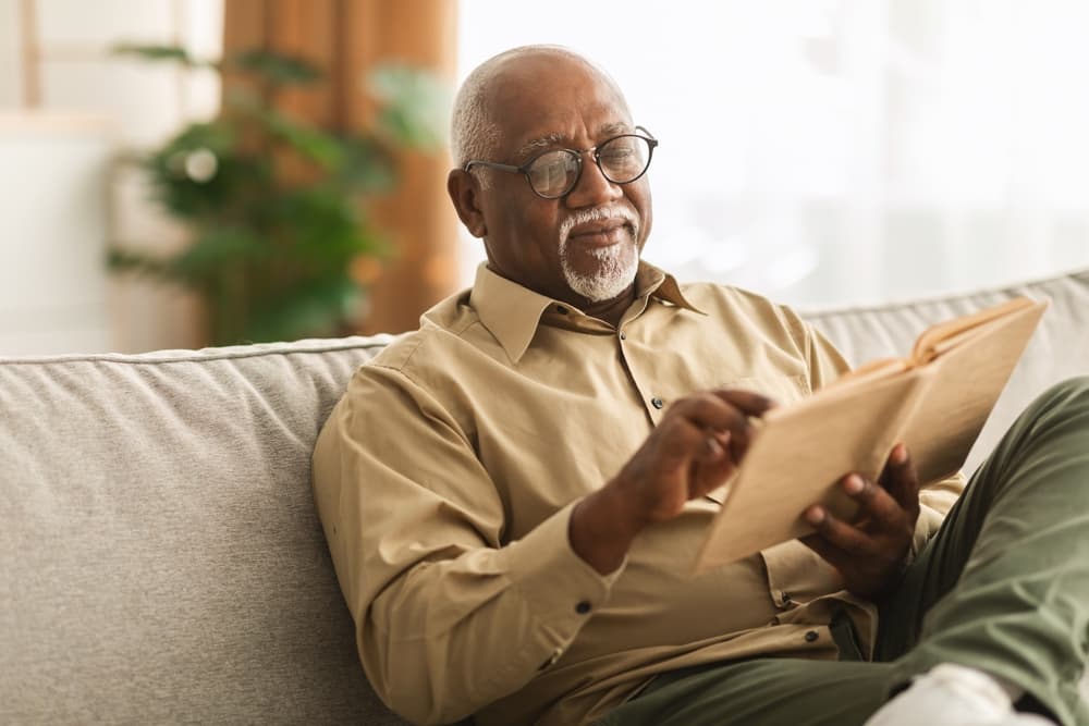 Senior,African,American,Man,Reading,Book,Sitting,On,Couch,At