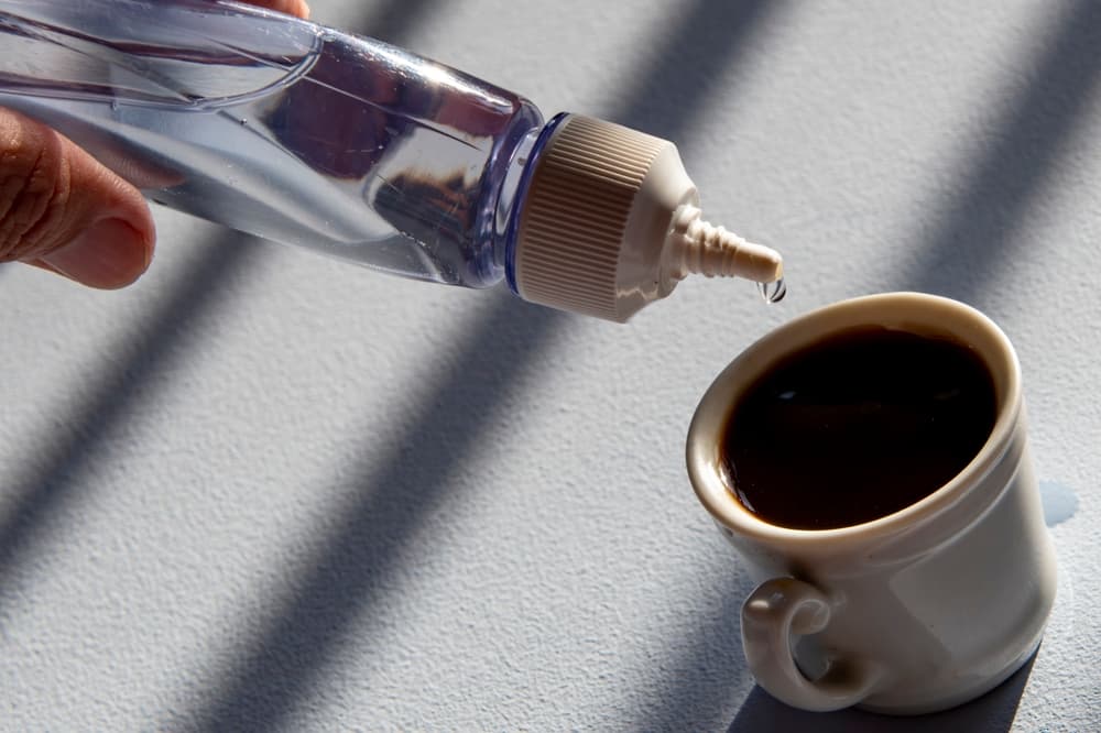 Person,Sweetening,Coffee,With,Liquid,Sweetener,,Scene,Showing,Cup,And
