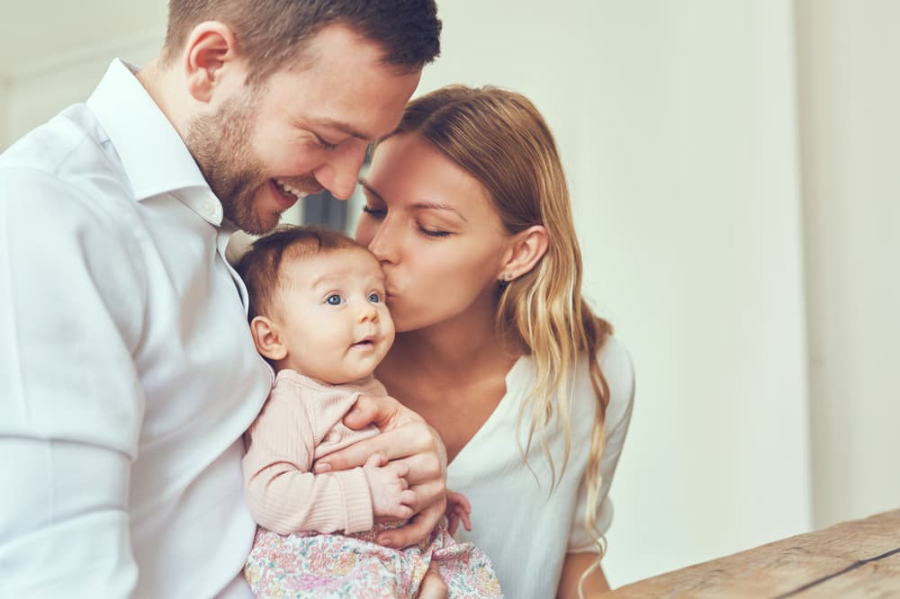 Smiling,Mother,And,Father,Holding,Their,Newborn,Baby,Daughter,At