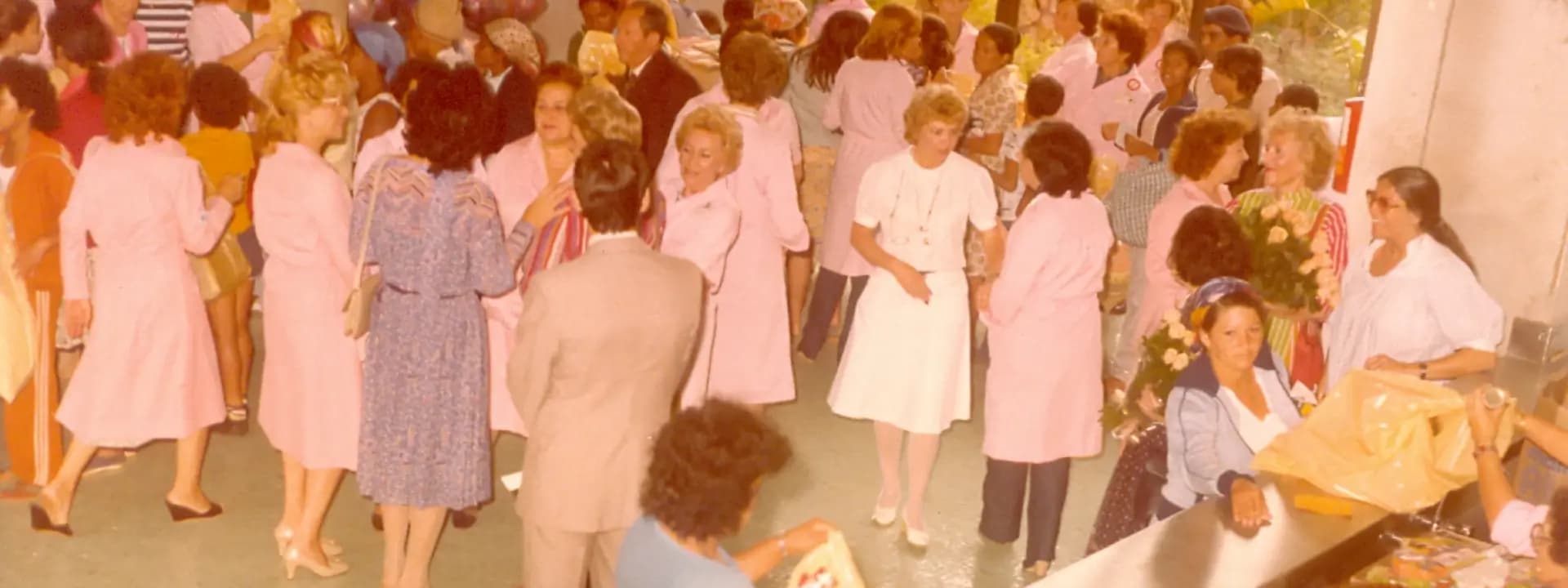 Fotografia histórica de um evento no Einstein com pessoas reunidas, muitas em jalecos cor de rosa, simboliza momentos marcantes e a memória institucional do compromisso com a saúde e a comunidade
