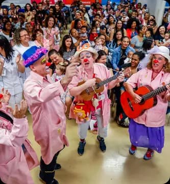 Grupo de voluntários do Einstein vestidos de palhaços tocando instrumentos e interagindo com pacientes e acompanhantes, representa o impacto positivo do voluntariado na humanização e acolhimento no ambiente hospitalar.