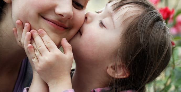 Criança com Síndrome de Down beijando a bochecha da mãe Criança com Síndrome de Down beijando a bochecha da mãe