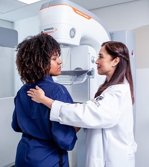 Enfermeira orienta paciente durante exame de mamografia, reforçando a importância da prevenção no Outubro Rosa contra o câncer de mama. Enfermeira orienta paciente durante exame de mamografia, reforçando a importância da prevenção no Outubro Rosa contra o câncer de mama.