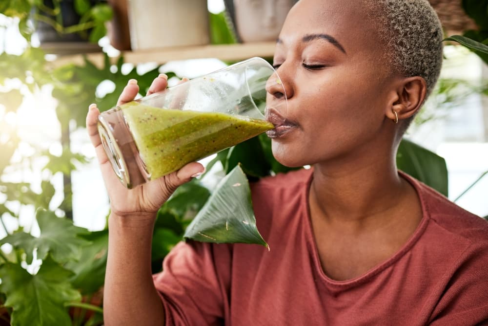 Pessoa tomando um suco verde, conhecido como detox, após uma refeição.