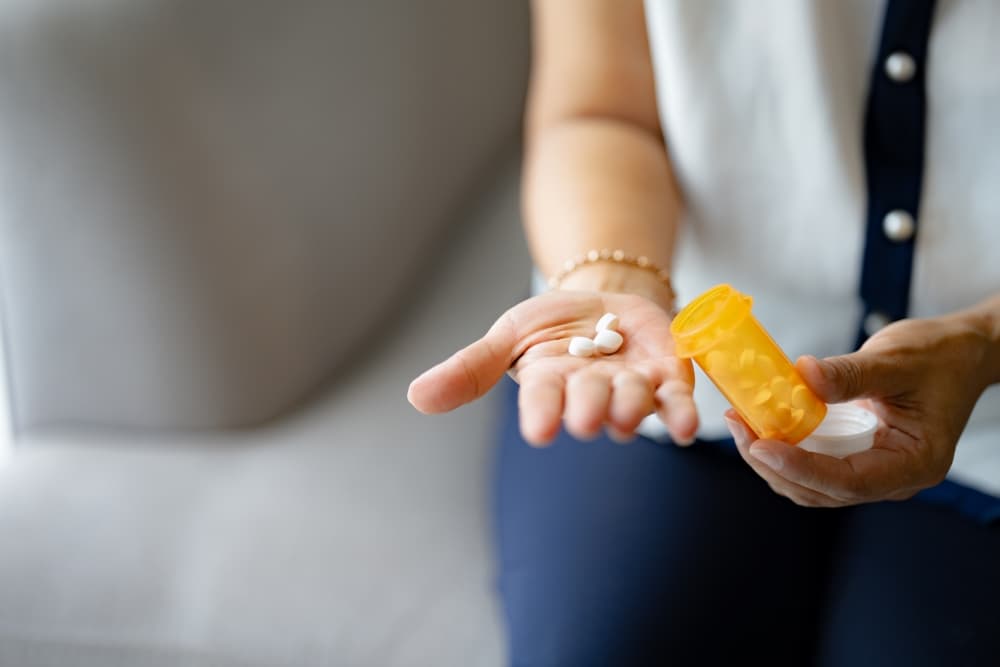 Uma pessoa segurando um frasco de medicamento na mão esquerda e alguns comprimidos na mão direita, em preparação para tomá-los.