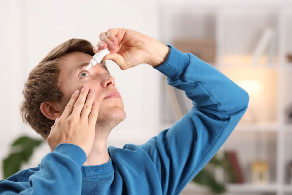 Pessoa com sintomas de conjuntivite pingando colírio em um dos olhos