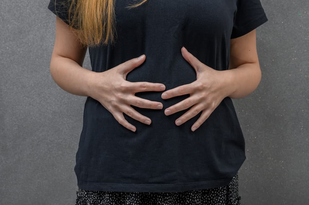 Uma pessoa com as duas mãos sobre a barriga inchada, sintoma da SII - Síndrome do intestino irritável