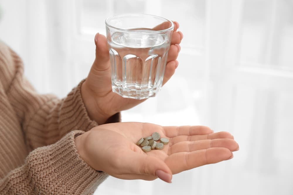 Uma pessoa com um copo com água para tomar junto com o medicamento Fenazopiridina que está em uma das suas mãos