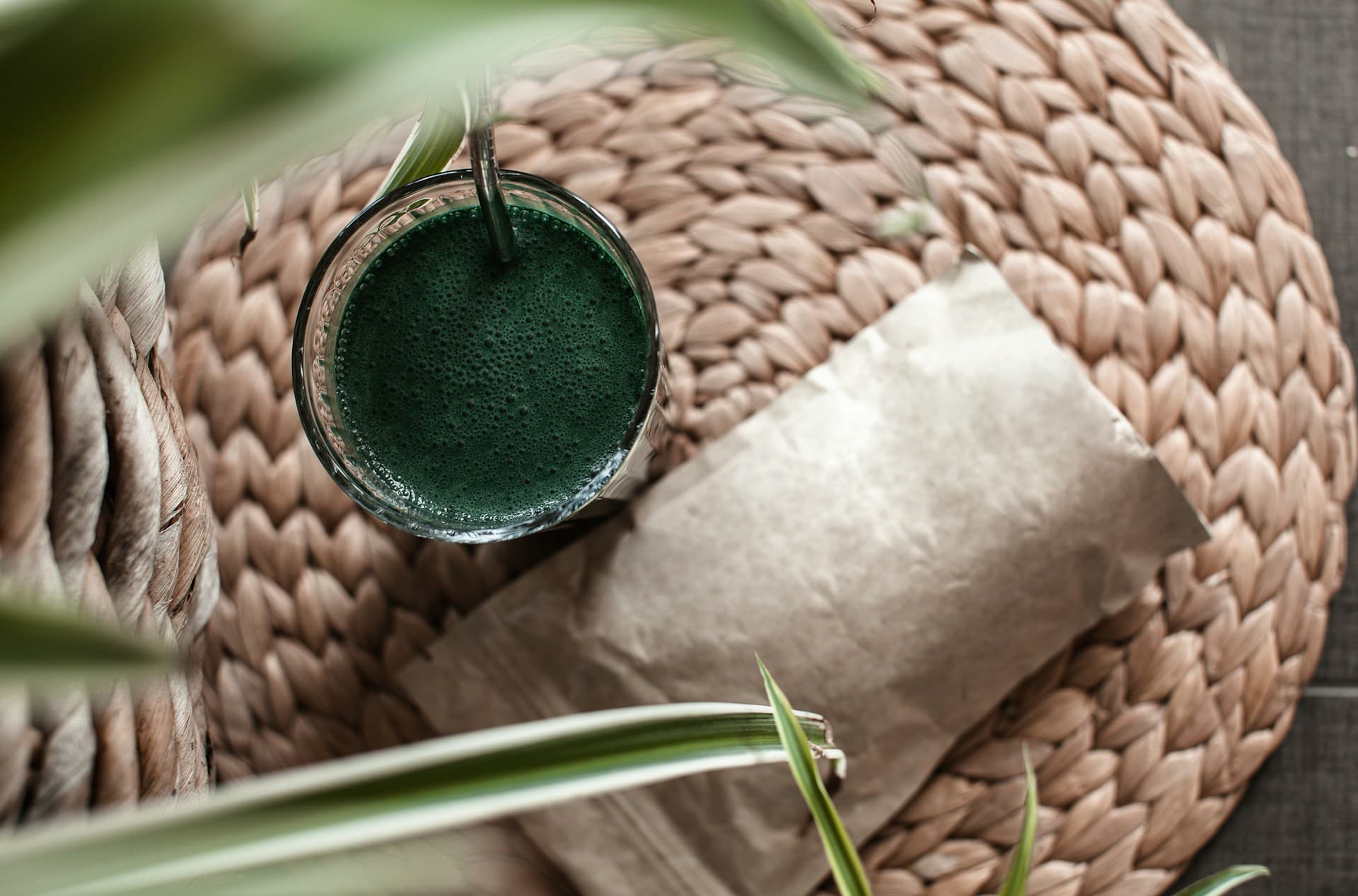Copo com suco verde de espirulina sobre esteira de palha.