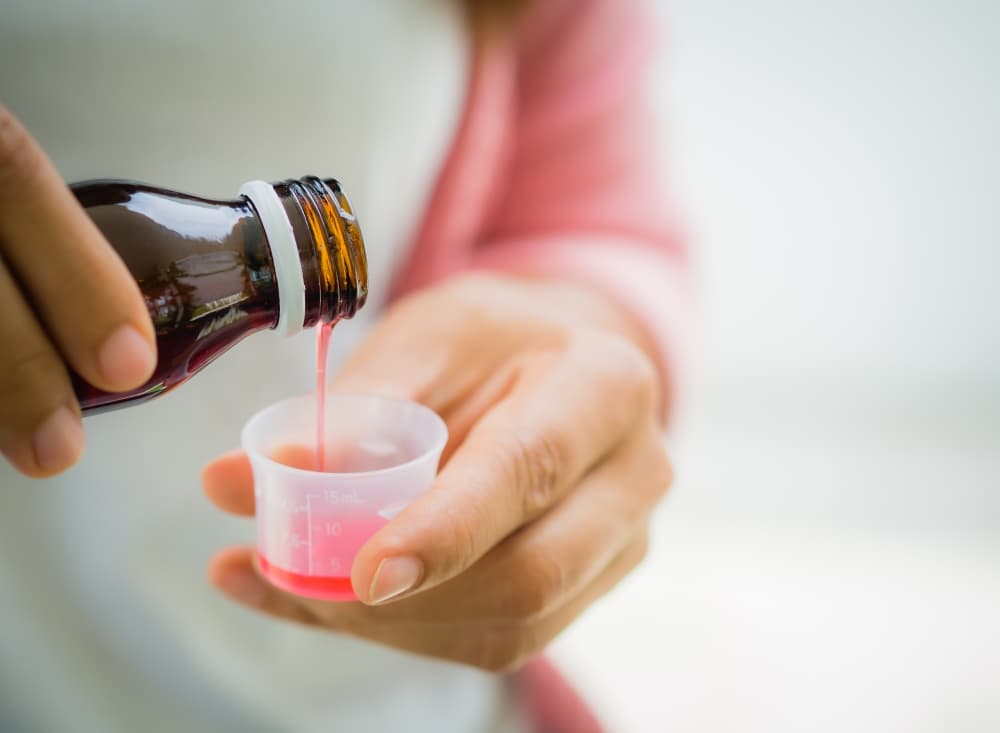 Uma pessoa utiliza o medidor de um xarope para dosar a quantidade exata do medicamento.
