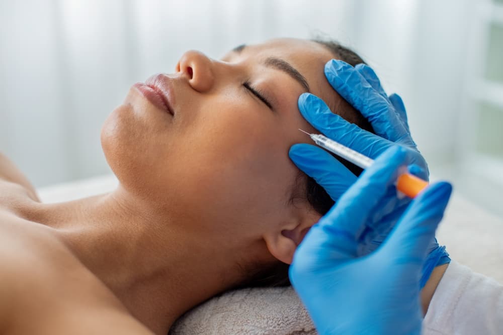 Uma profissional em harmonização aplicando uma solução injetável na região dos olhos de uma paciente.