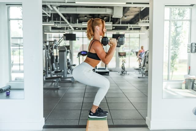 Uma aluna em um espaço dedicado a exercícios físicos executando os movimento de agachamento com peso