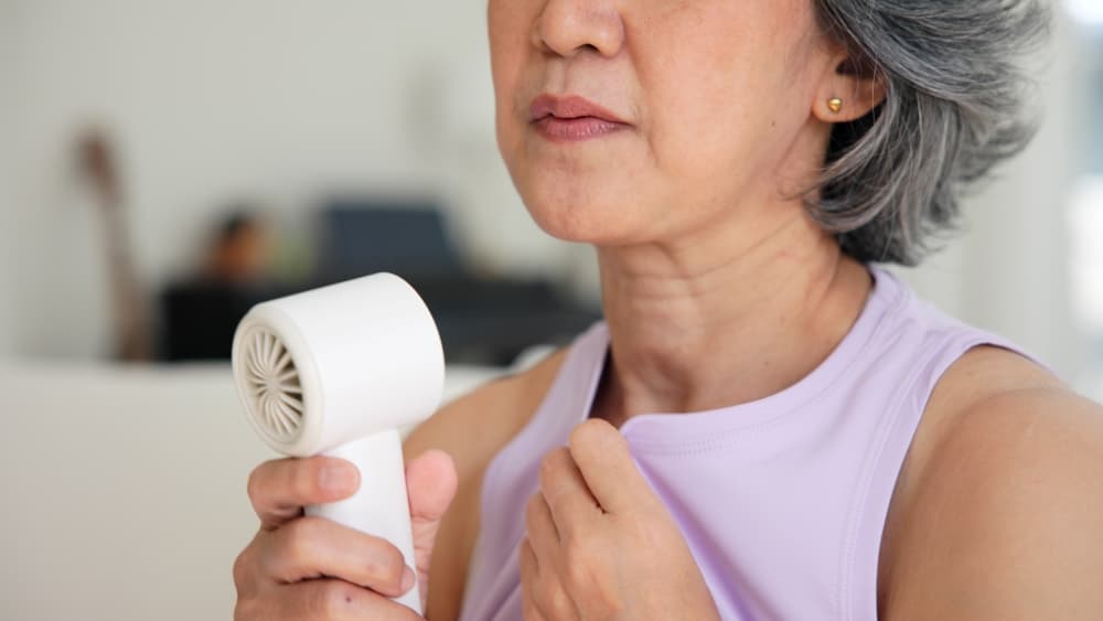 Uma mulher utilizando um ventilador portátil por causa as ondas de calor da menopausa