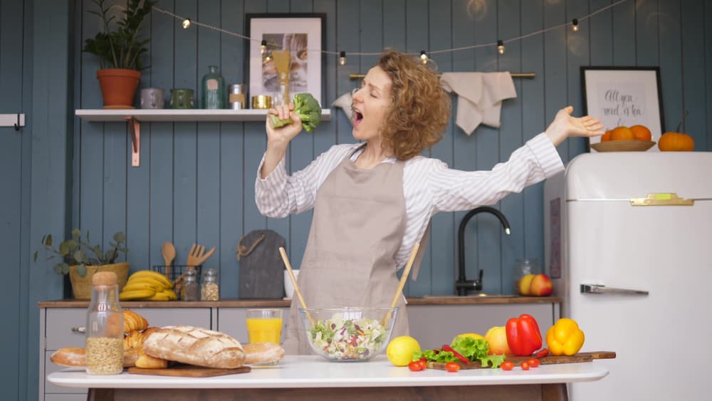 Young,Happy,Woman,Singing,And,Dancing,On,Kitchen,While,Cooking