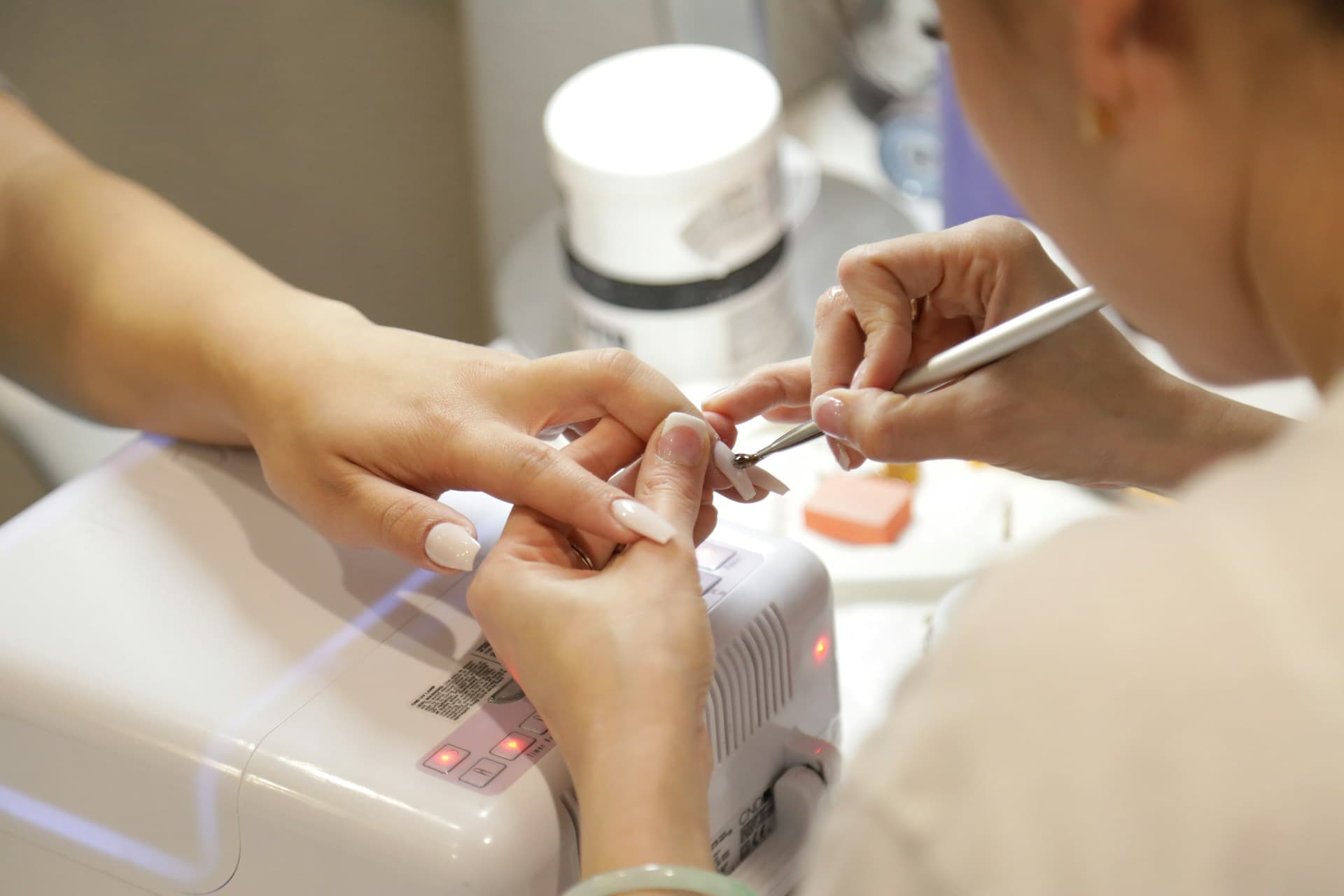 Profissional de estética efetuando procedimentos nas unhas de uma clientes em um estúdio com equipamentos adequados