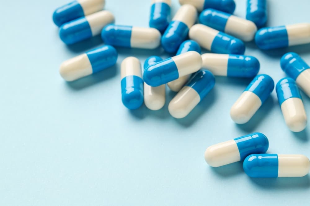 Cápsulas de medicamentos espalhados sobre uma superfície azul claro.