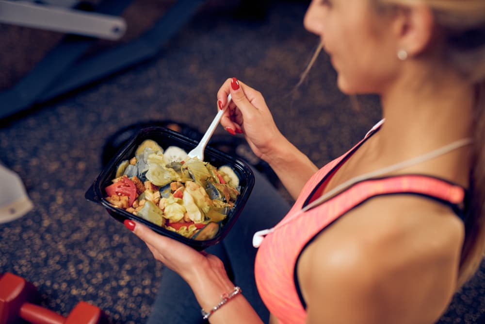 Pessoa vestindo roupa de academia, alimentando-se com uma grande porção de comida.