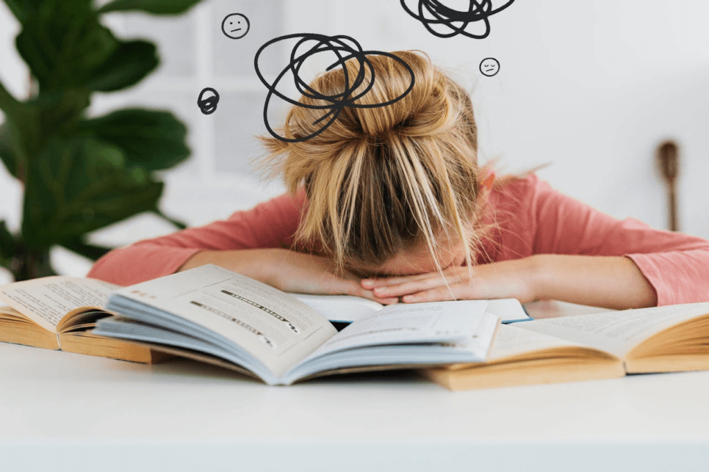 Pessoa debruçada sobre livros abertos em uma mesa, sinal evidente de esgotamento mental relacionado com burnout