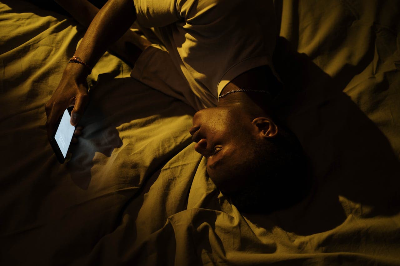 Pessoa deitada na cama utilizando um dispositivo mobile por não conseguir dormir.