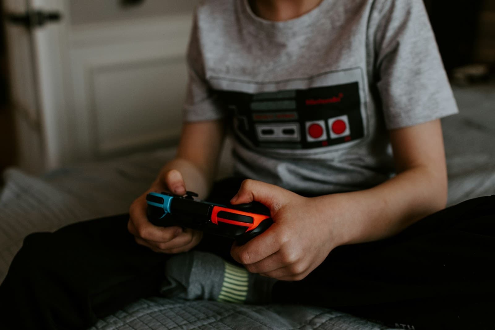 Uma criança sentada, com uma estampa de um controle retrô de videogame, segurando um controle de videogame.