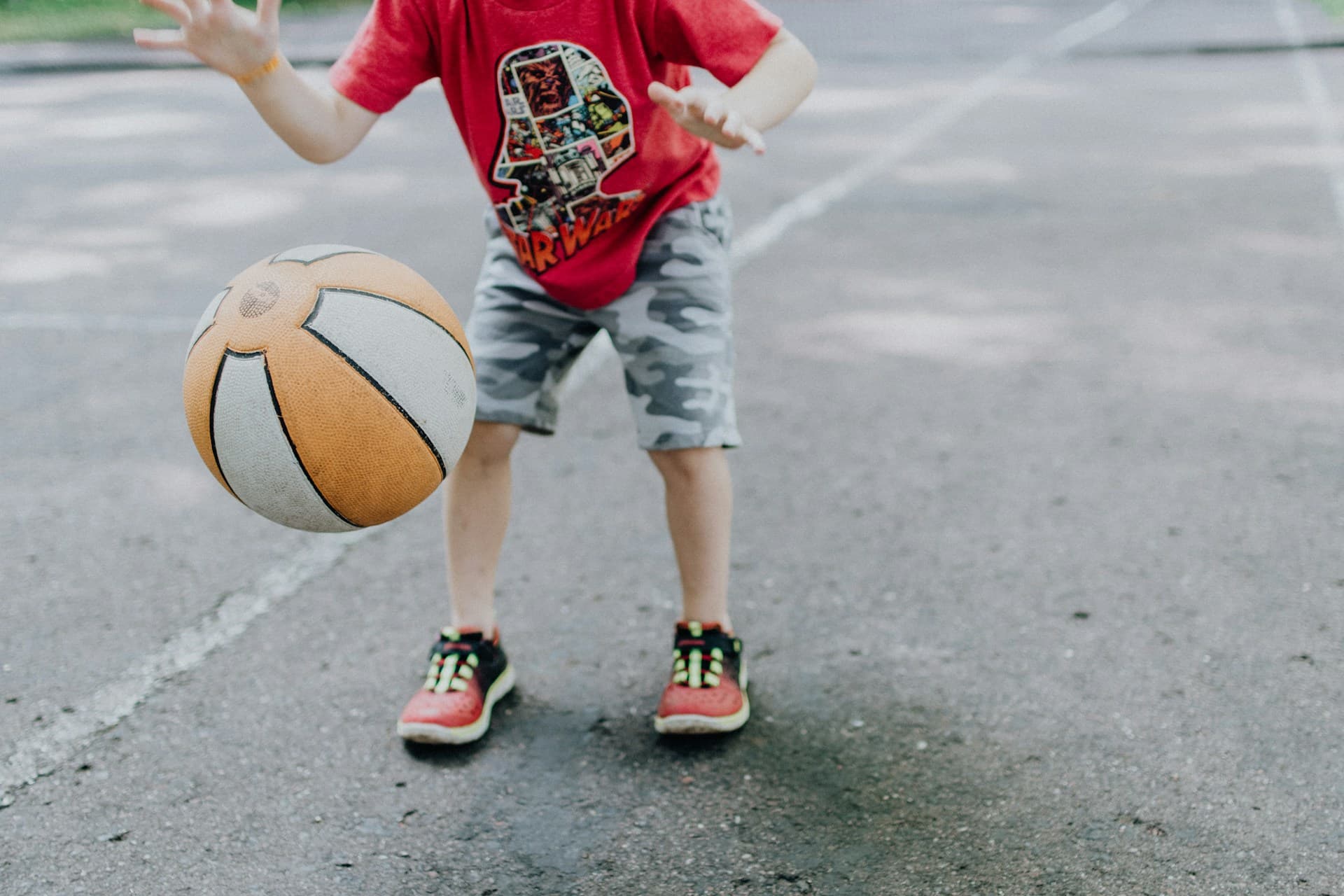 Uma criança em um local de prática de atividade física e esportes com uma bola de basquete.