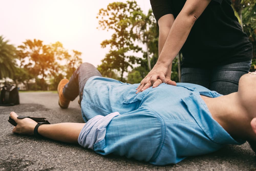 Pessoa deitada no chão recebendo massagem cardíaca por uma pessoa preparada com as técnica correta de reanimação em casos de infarto