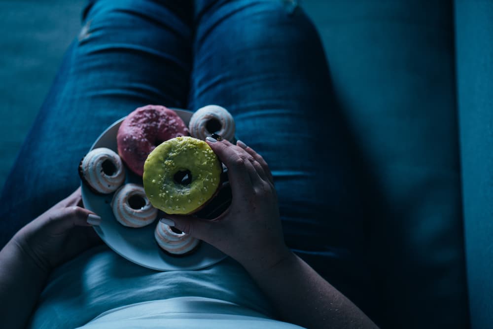 Pessoal deitada em um sofá com um prato com doces coloridos em forma de rosquinhas.