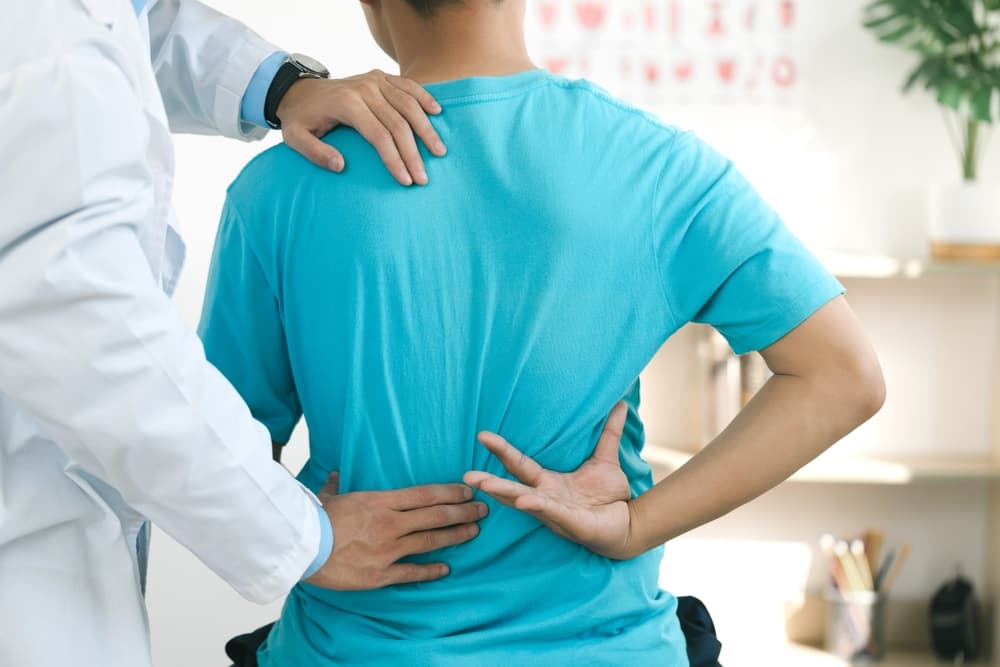 Profissional da saúde fazendo exame clínico em uma pessoas com sinais de dores nas costas, o profissional está com a mão na região lombar.