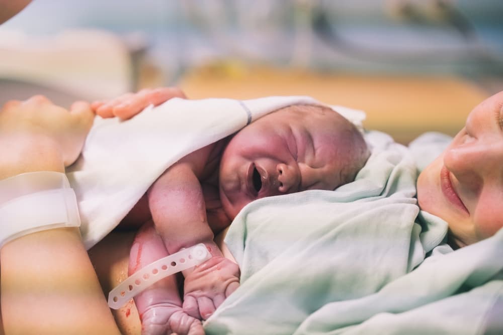 Mãe com o bebê (RN) recém-nascido no colo logo após o nascimento.