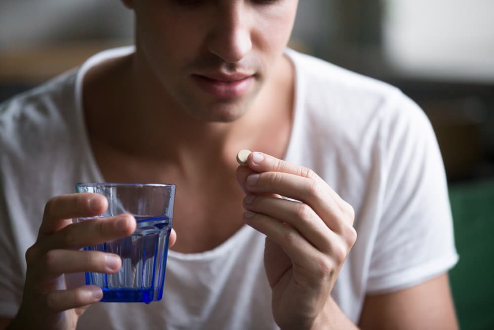 Pessoa com um copo de água na mão direita e, com a mão esquerda, levando o medicamento Fluoxetina à boca.