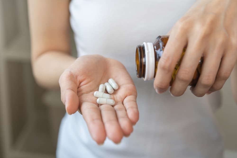 Pessoa segurando cápsulas de medicamento com a mão direita e o frasco aberto na mão esquerda.