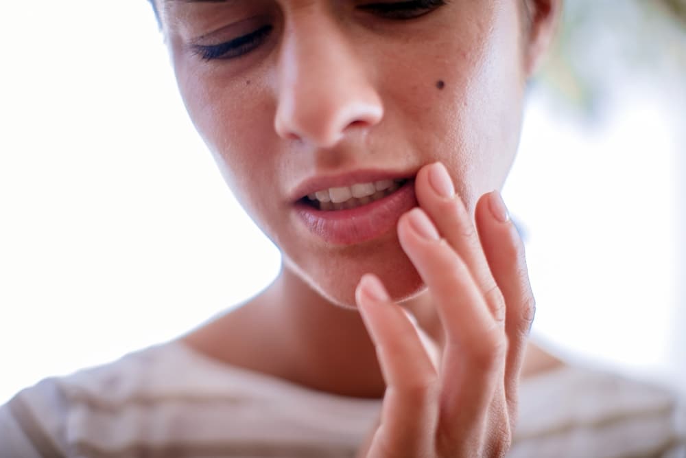 Uma pessoa com a mão no canta na boca, sensação de incômodo causado pelo vírus do herpes tipo1.