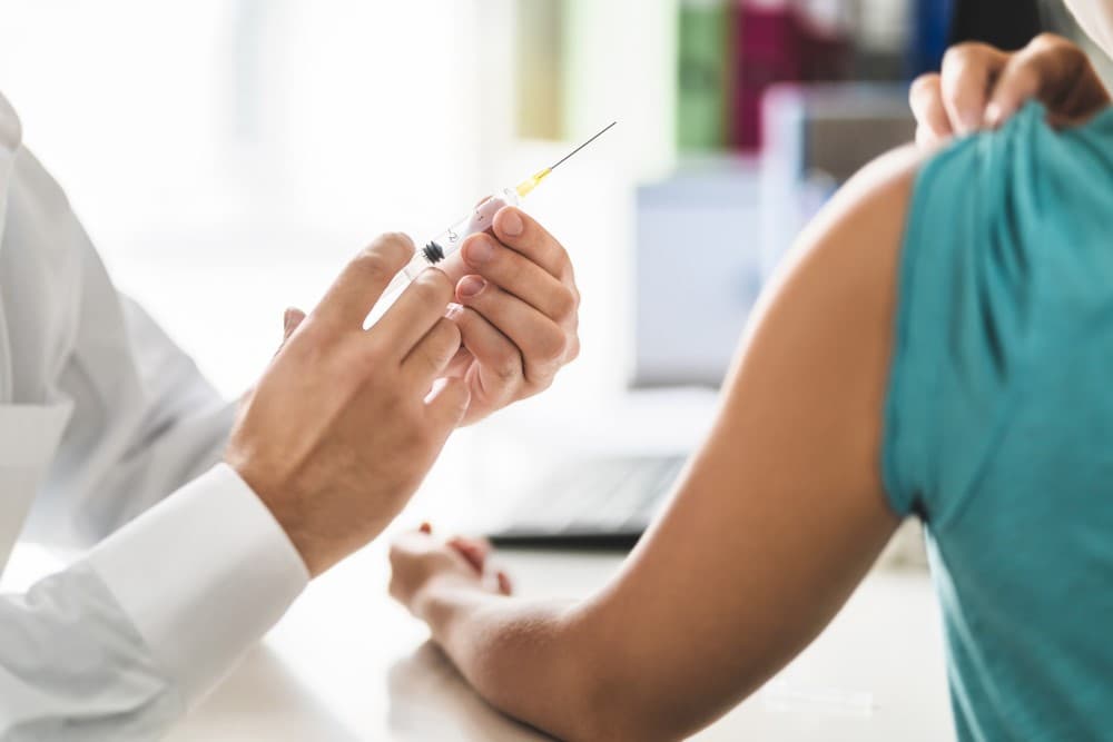 rofissional de Saúde preparando uma seringa para aplicar a vacina contra HPV em uma pessoa.