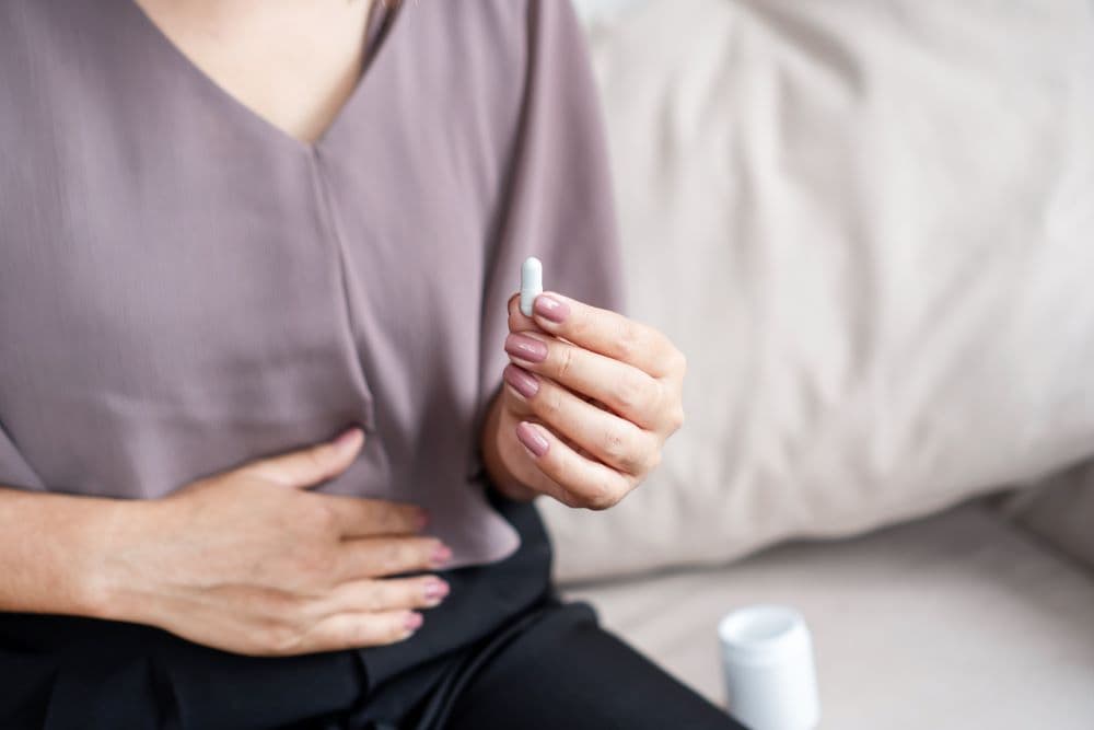 Uma pessoa com a mão na região do abdômen devido ao desconforto gástrico, preparando-se para tomar medicamento
