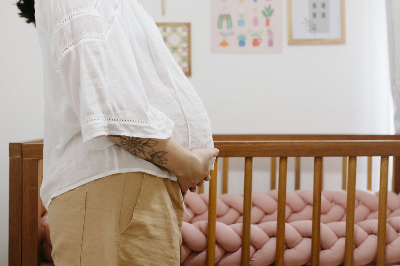 Pessoa grávida em quarto de bebê em frente ao berço.
