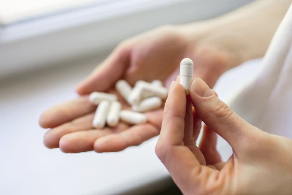 Pessoa com uma porção de medicamentos na mão direita e segurando uma cápsula com na mão esquerda demonstrando que irá tomar o medicamento.