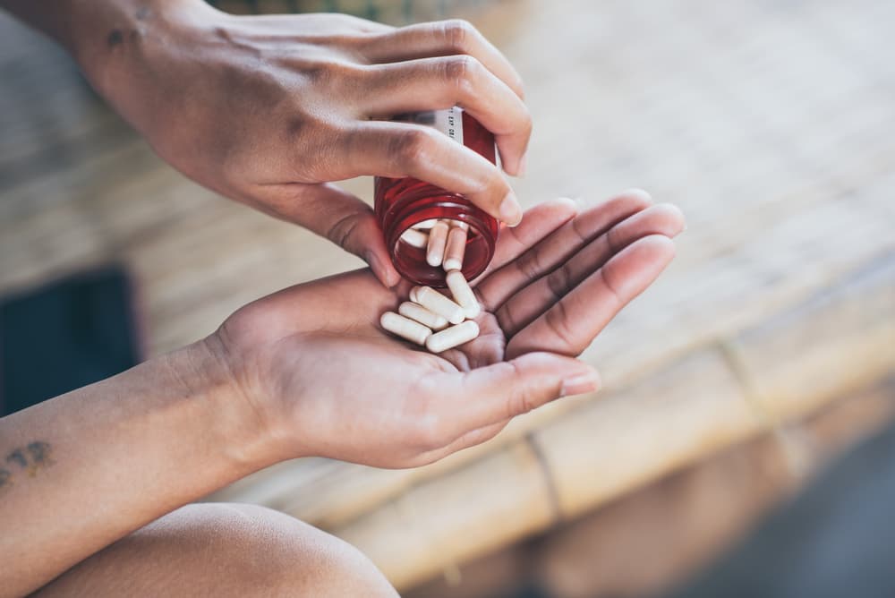 Pessoa com um frasco de remédio na mão esquerda e com capsulas na mão direita