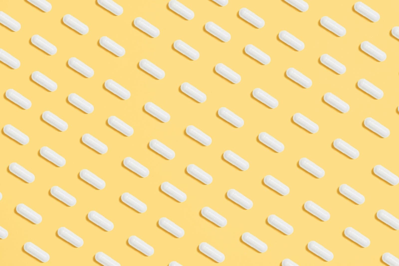 Imagem com fundo amarelo com várias cápsulas de medicamentos distribuídas de forma simétrica