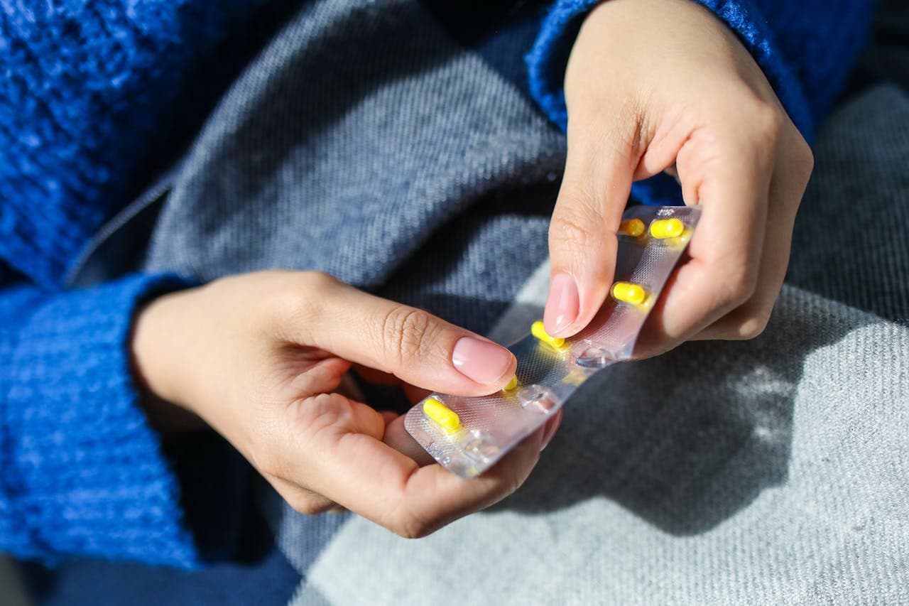 Pessoa com uma cartela de medicamentos nas mãos, está retirando uma unidade de paracetamol para ingerir.