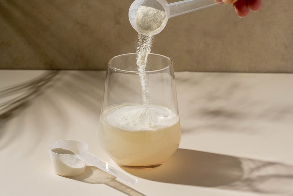 Em uma mesa branca, um copo de vidro com água e dois scoops de suplemento dextrose