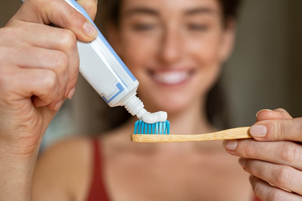 Pessoa aplicando o creme dental em uma escova de dentes.