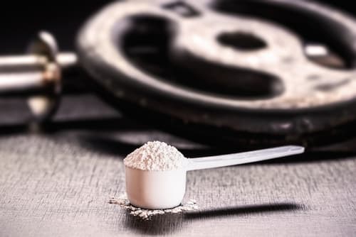 Um scoop de creatina em uma mesa com halteres de musculação