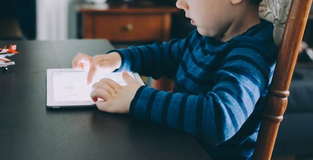 Criança sentada à mesa interagindo com um dispositivo do tipo tablet.