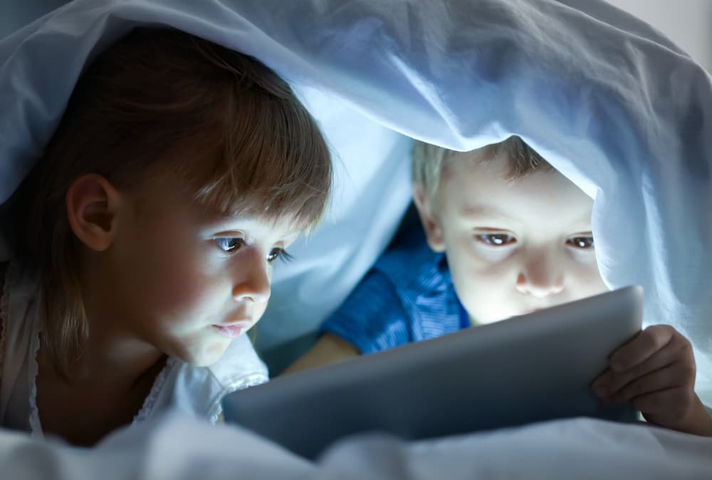 Cute,Little,Children,Lying,Under,Blanket,With,Tablet,Computer