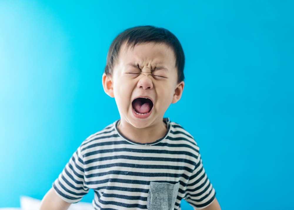 Criança demonstrando insatisfação, com semblante de choro e expressão facial de gritos.